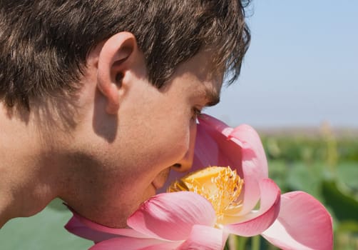 Young man smelling a pink lotus, close-up