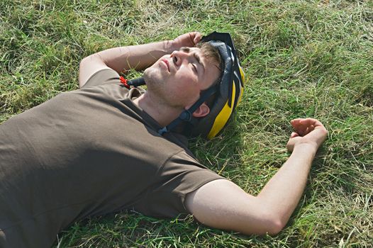 Young cyclist lying on a ground with eyes closed