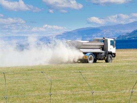 Truck spreading fertilizer on pasture meadow creating an enormous white dust cloud of rock phosphate and potash