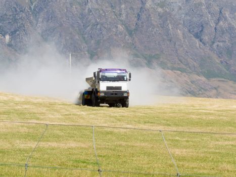 Truck spreading fertilizer on pasture meadow creating an enormous white dust cloud of rock phosphate and potash