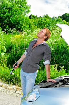 Young man repairing broken car with a socket spanner wrench.