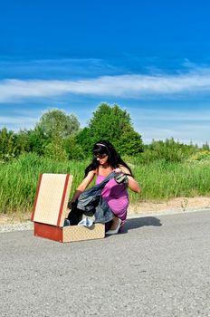 Woman on a road getting clothes from suitcase.