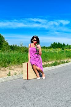 Woman with rose sitting on suitcase on the road.