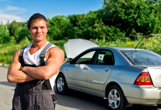 Handsome mechanic on a road near the broken car.