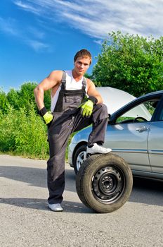 Handsome mechanic standing on a tire on the road