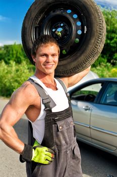 Portrait of a handsome mechanic holding a tire on shoulder