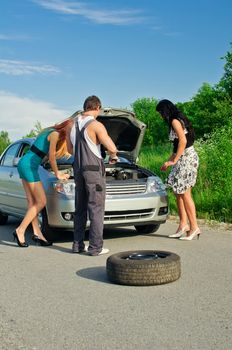 Mechanic and two girls near the broken car on a road