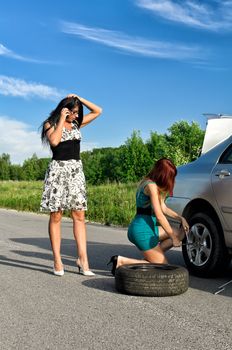Two women are changing a tire on a road