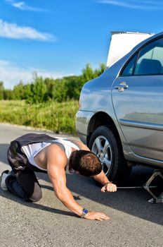 Mechanic sets a jack-screw under the car on a road
