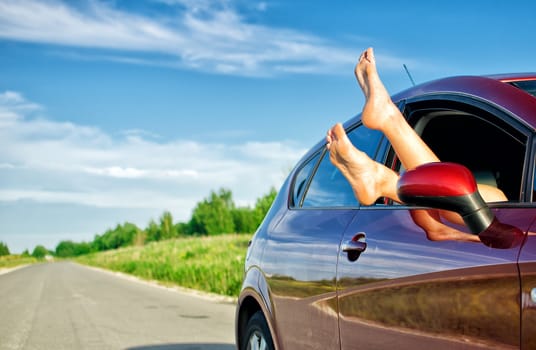 Woman's legs out of the car window. Concept of carefree funny trip.