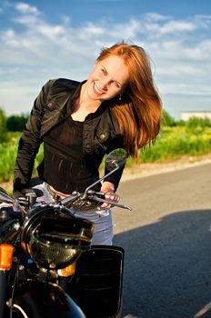 Smiling redhead girl on a motorbike on a road