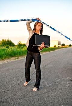 Young criminalist with laptop crossing police tape