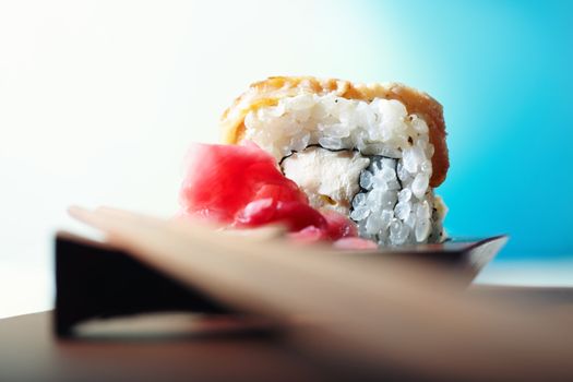 Close-up horizontal photo of the rolled sushi with ginger on the table and chopsticks. Shallow depth of field and vivid colors