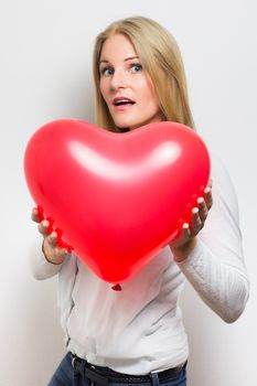 Surprised  caucasian woman holding a red heart balloon
