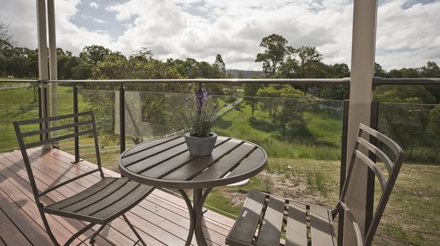 Wooden table and chairs on a glassed in timber deck overlooking green countryside