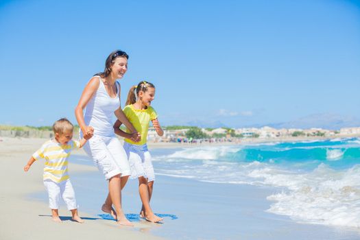 Happy family of three - mother and her child running and having fun on tropical beach