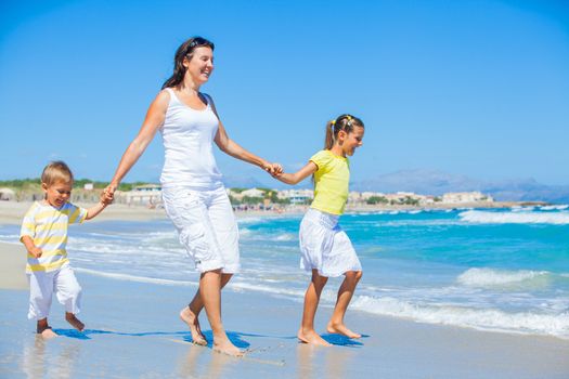 Happy family of three - mother and her child running and having fun on tropical beach