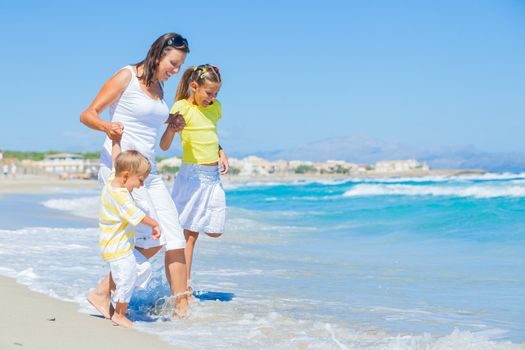 Happy family of three - mother and her child running and having fun on tropical beach