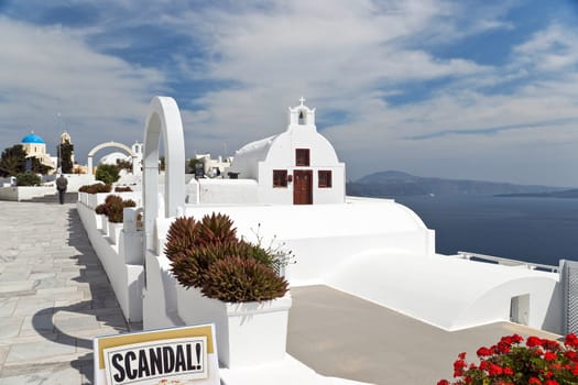 Santorini whitewashed church above Caldera with tablet "Scandal!" in front