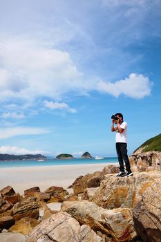 Portrait of a young man standing on a beach with a camera 