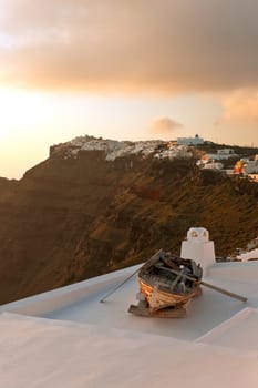 Sunset in Santorini island with the boat in the front and buildings on the rock
