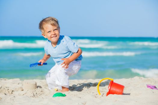 Cute baby boy playing with beach toys on tropical beach