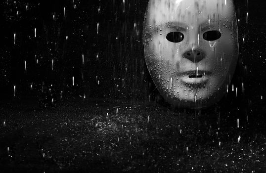 Plastic mask under the rain on a dark background