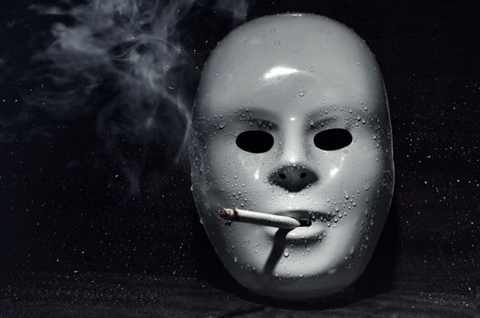 Plastic mask smoking tobacco or hashish on a dark background