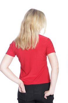 Back view of a young blond woman dressed in black jeans and a red top standing with her hands in her pockets isolated on white