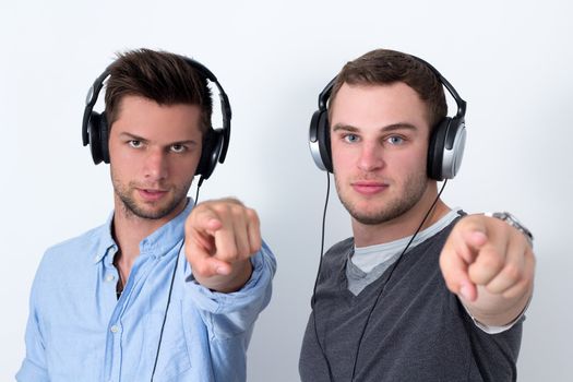 Two friends with headphone listening to music in front of a white background and pointing at camera