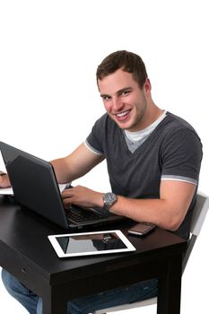 Happy man using pc and smiling while sitting at table with tablet on mobile phone lying on it