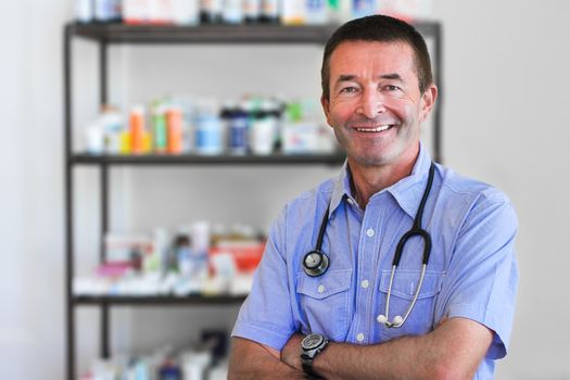 Mature Doctor Standing In Front Of A Shelf Full Of Medicine