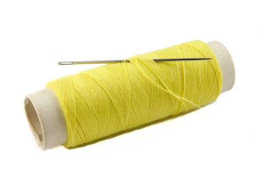 yellow thread bobbin with needle on white background