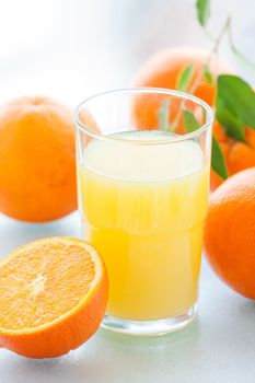 Glass of juice and sliced and whole orange with green leaves