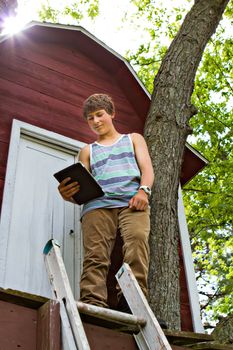 Teenager  reading a touchpad  infront of a Treehouse