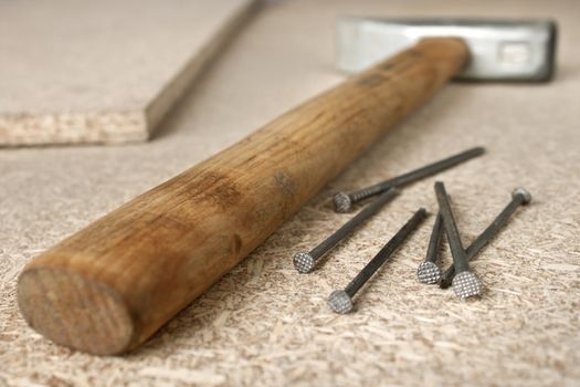 Hammer and a handful of nails are on chipboard