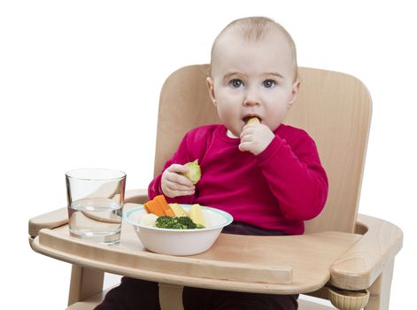 young child in red shirt eating vegetables in wooden chair.
