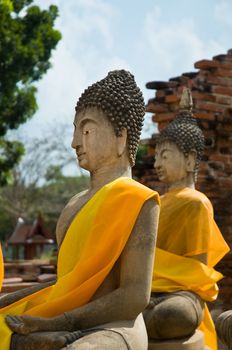 Two Buddha statues wrapped in an orange scarf. Ayutthaya city is the capital of Ayutthaya province in Thailand. Its historical park is a UNESCO world heritage.