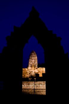 Iluminated Stupa under a dark blue night sky view through a stone gate in Ayutthaya. Ayutthaya city is the capital of Ayutthaya province in Thailand. Its historical park is a UNESCO world heritage.