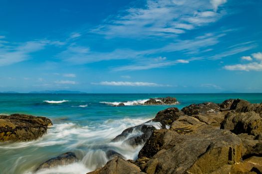 Sea landscape with rock beach coastline, blue sky, long exposure, incoming waves