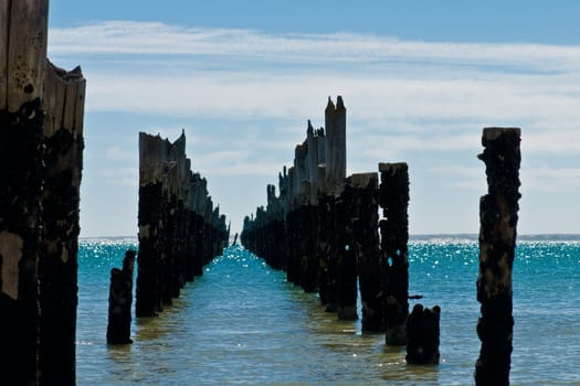 Beautiful rotten mooring on a beach where only the pillars are left over at a bright sunny day, view along the old construction