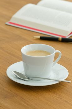 White coffee cup with open book and pen on a wooden table