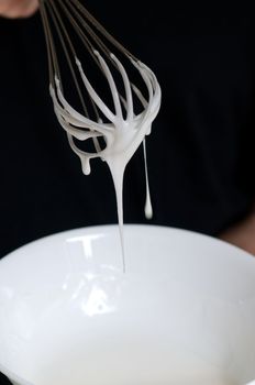 Whisk with creamy egg white close up flowing nicely down, over bowl