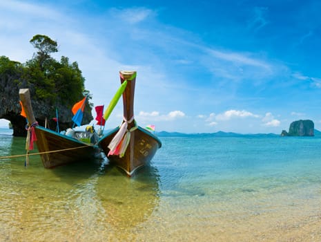 A long tail boat by the beach in Thailand green mountains and blue sky