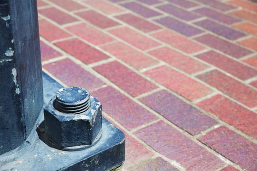 Close up of a lamp post bolt and nut with soft focus brick sidewalk background