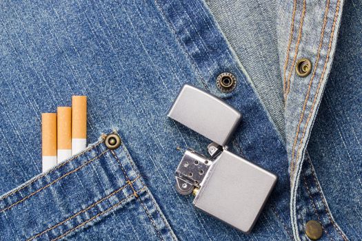 Close-up photograph of cigarettes and a silver light on a denim background.