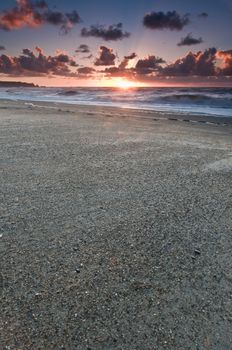 A beach during sunset with glowing sky with dark clouds