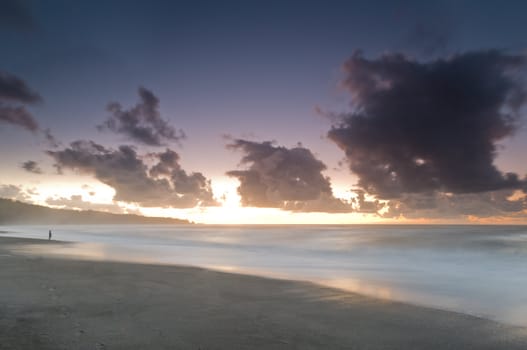 A beach during misty sunset with glowing sky and dark clouds