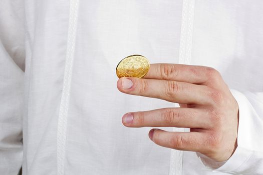 Close-up photograph of a golden coin between a man's fingers.