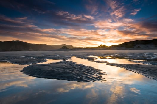 Sunrise above beach with reflection on incoming tide